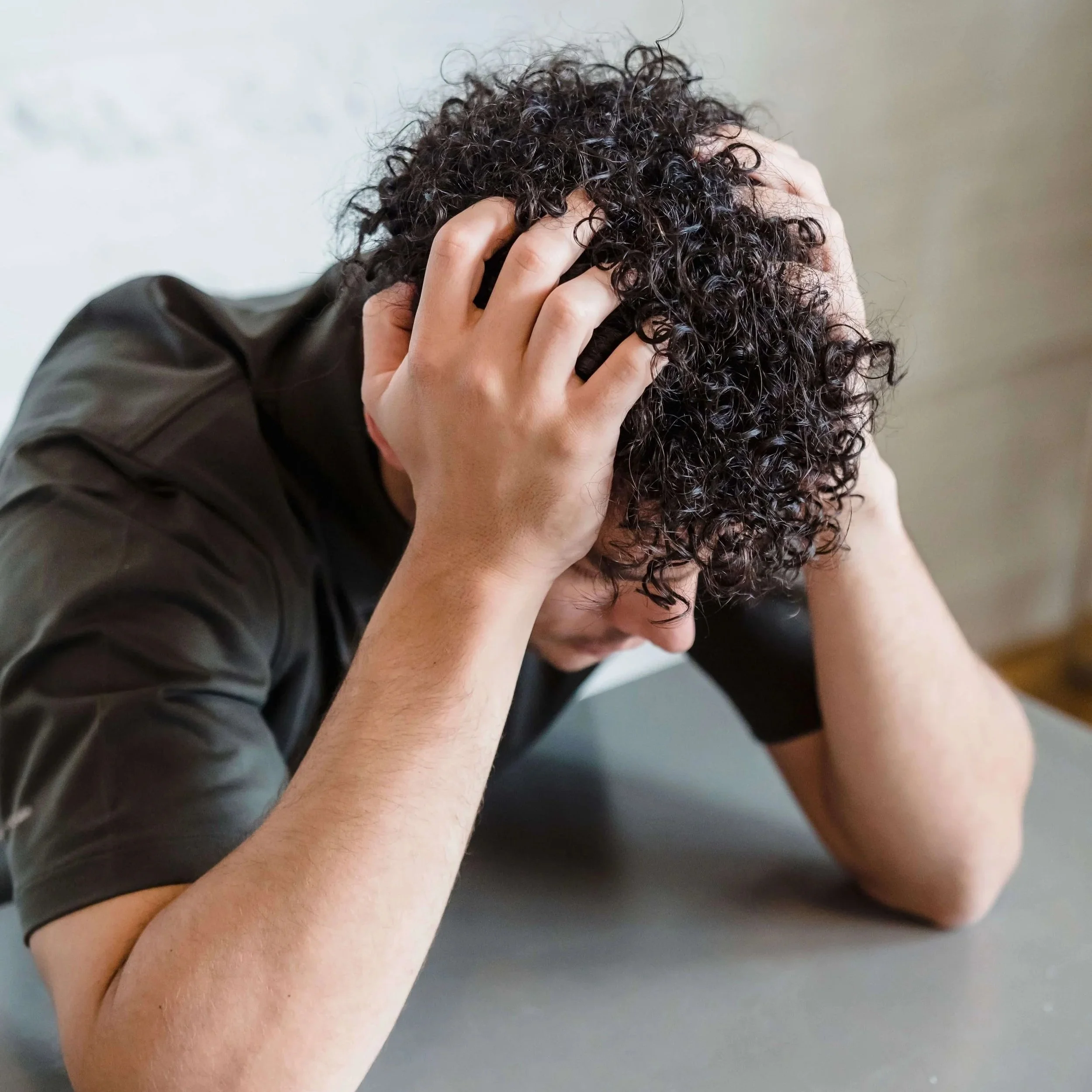 Man with curly dark hair hunched over a table gripping his head.Chronic anxiety often has deeper roots and anxiety therapy in Asheville, NC can help you finally get there.