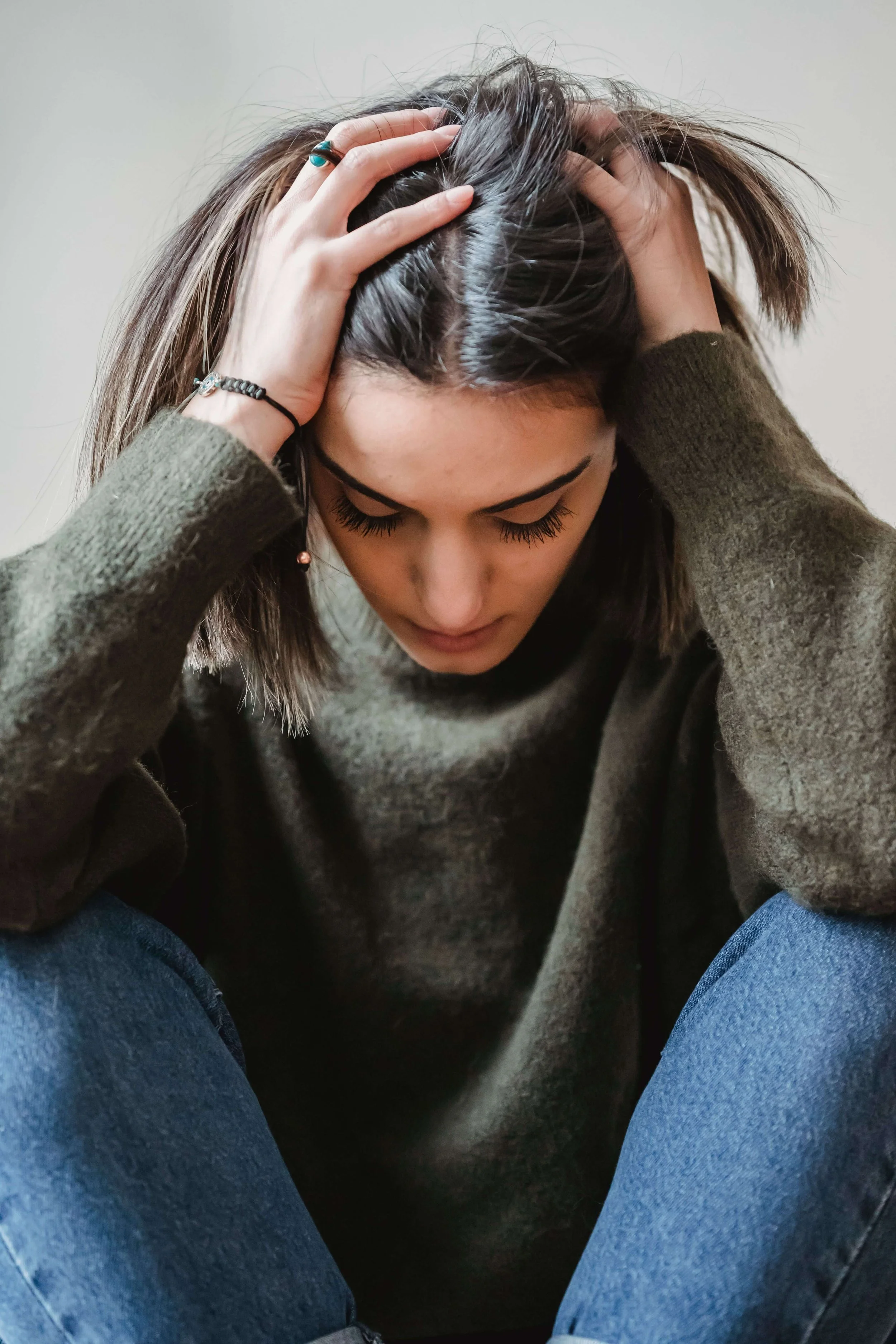 Woman in green sweater gripping her hair looking down. Anxiety doesn't have to keep running your life and online anxiety treatment in North Carolina can help.