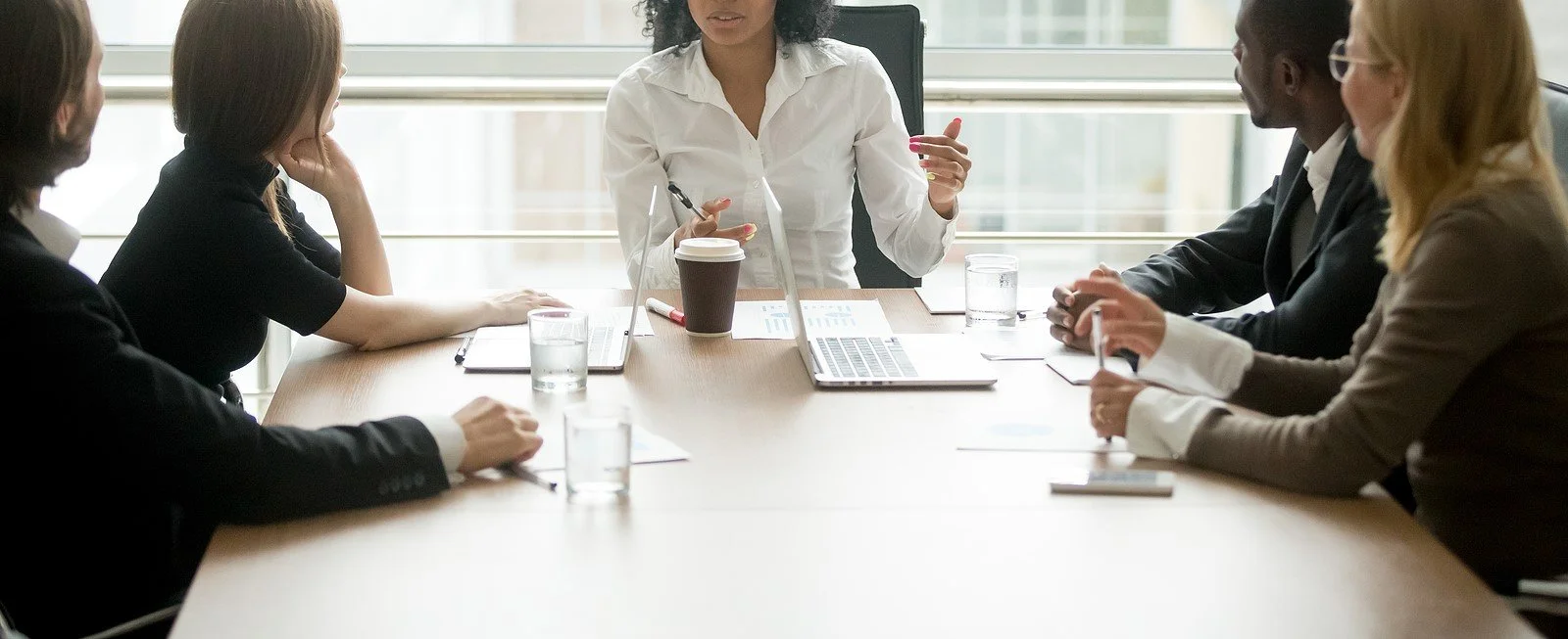 A woman sitting at the head of a conference table listens to coworkers as they talk. Learn more about online therapy in Asheville, NC by contacting an Asheville mental health therapist.