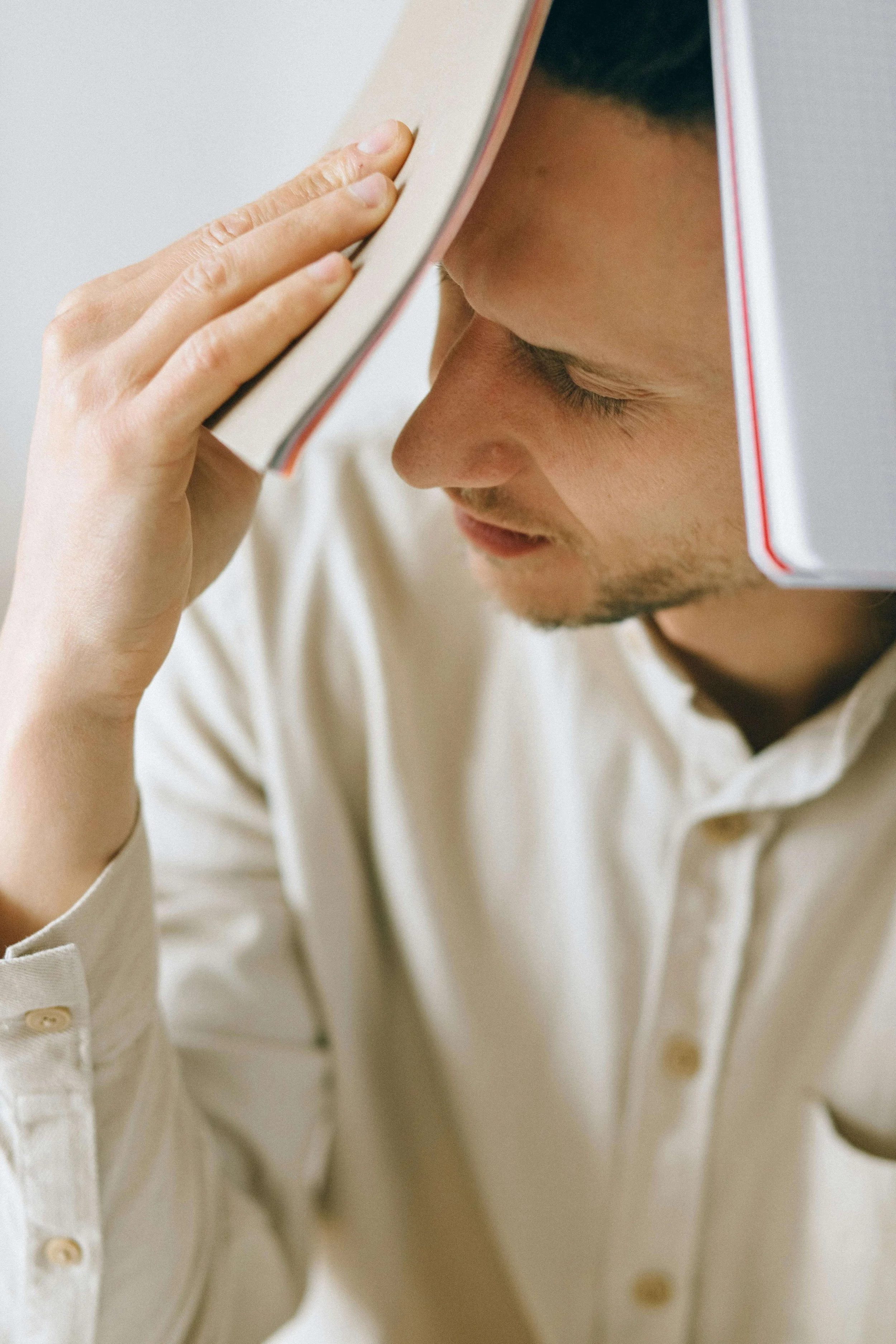 A young man pressing an open book against his forehead with his eyes closed. You don't have to figure out anxiety on your own and online anxiety treatment in North Carolina connects you with expert support no matter where you are.