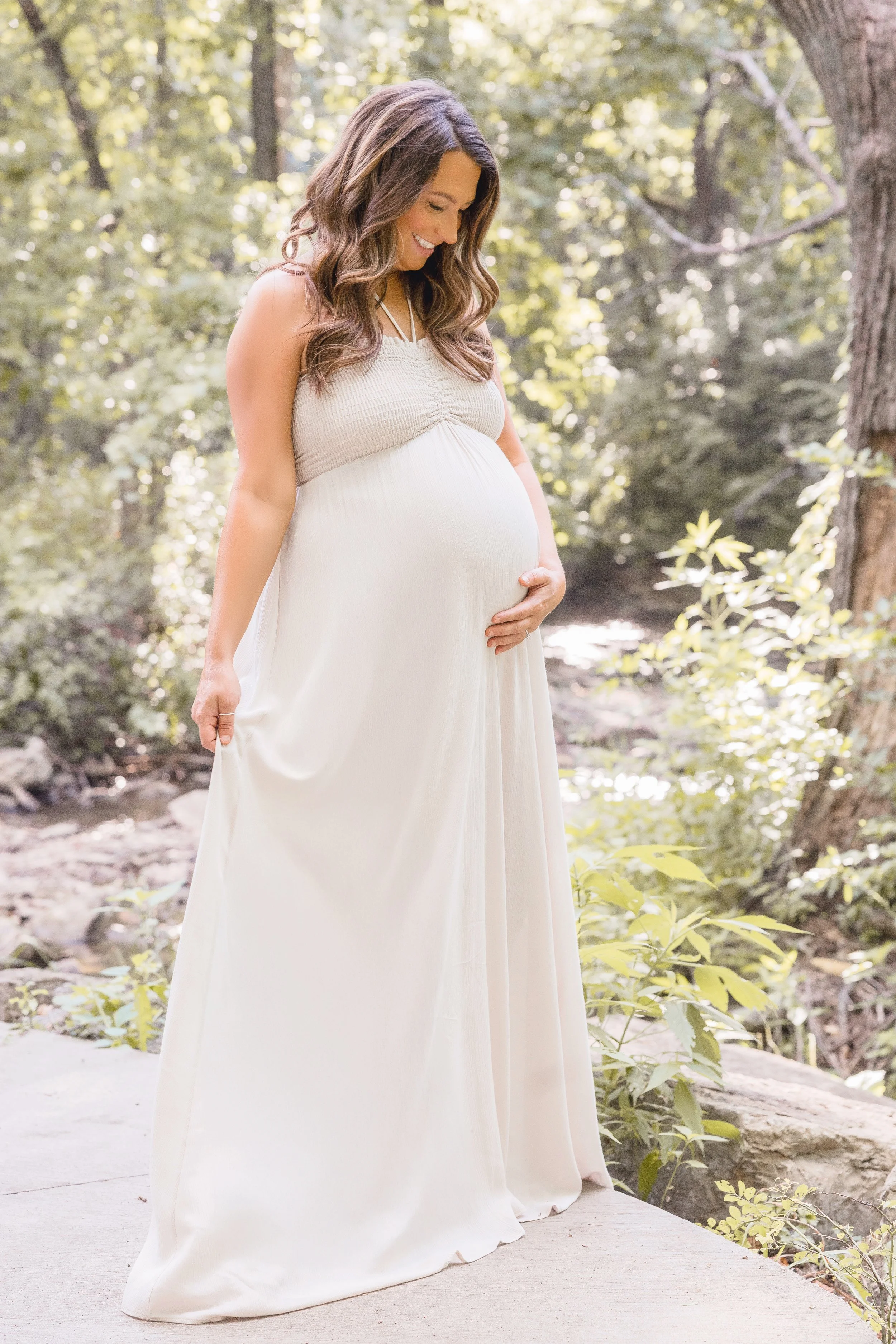 Backlit summer maternity portraits in Kansas City, expecting mother in flowing gown at Shawnee Mission Park