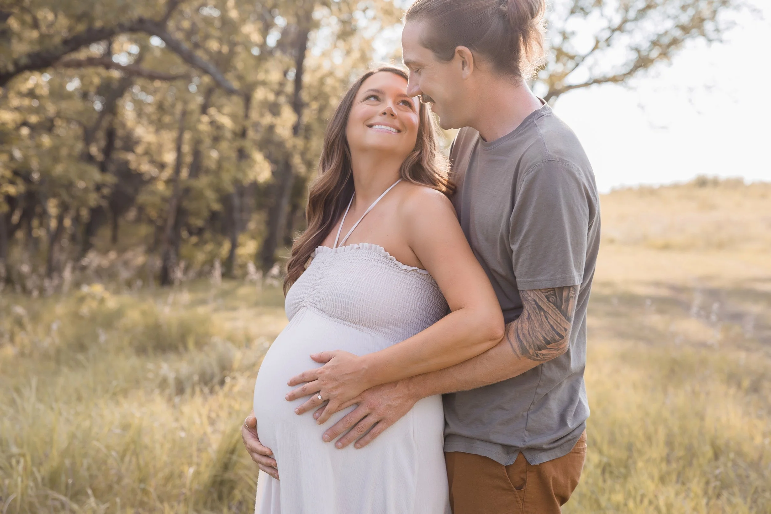 Kansas City maternity photography, husband holding wife close in golden evening light at Shawnee Mission Park