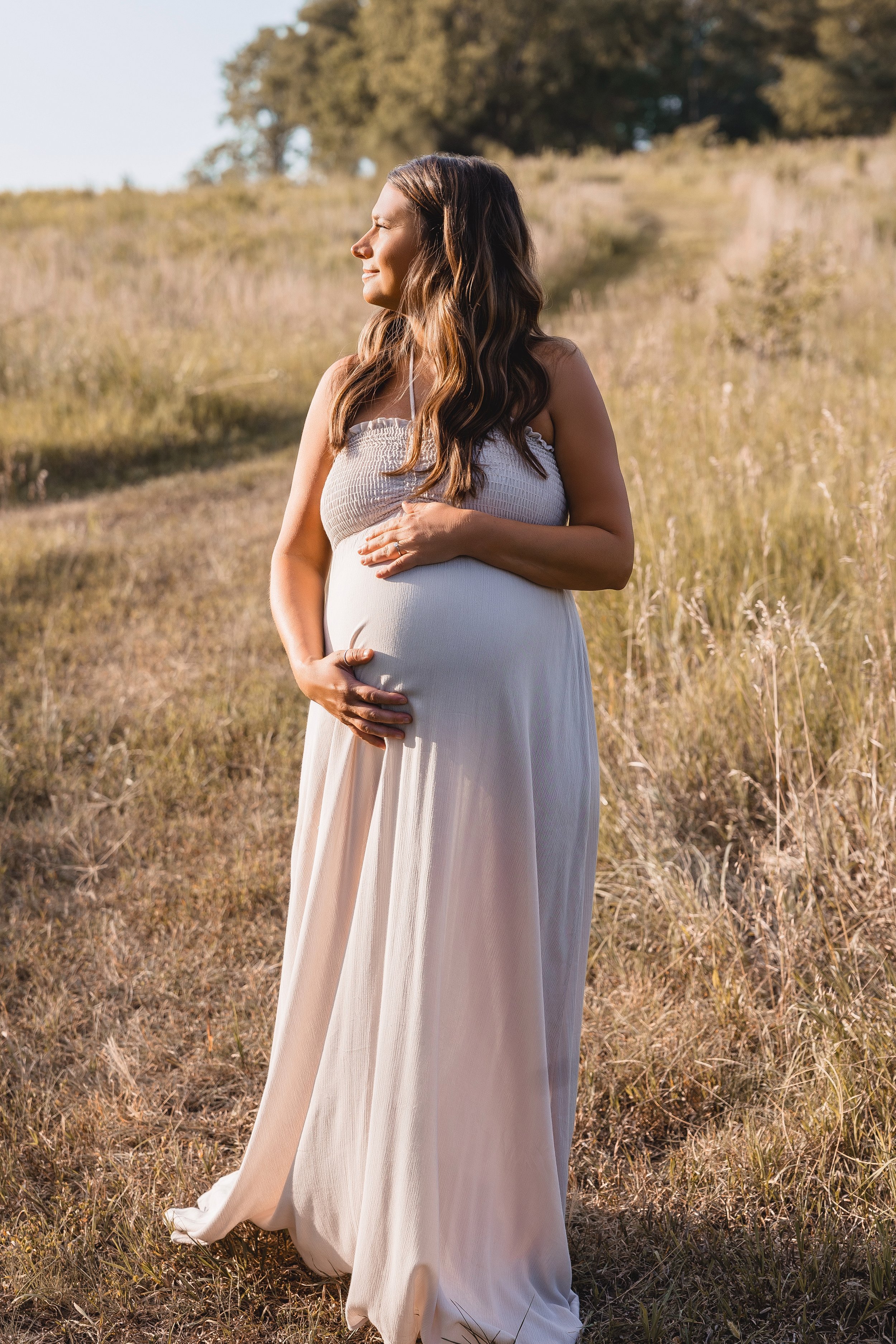 Golden summer maternity portrait in Kansas City, expecting mother holding baby bump at Shawnee Mission Park