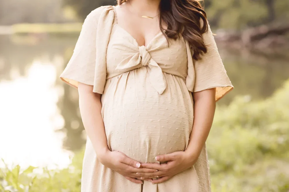 Outdoor maternity photography session in Kansas City featuring a mother in a neutral dress during golden hour.