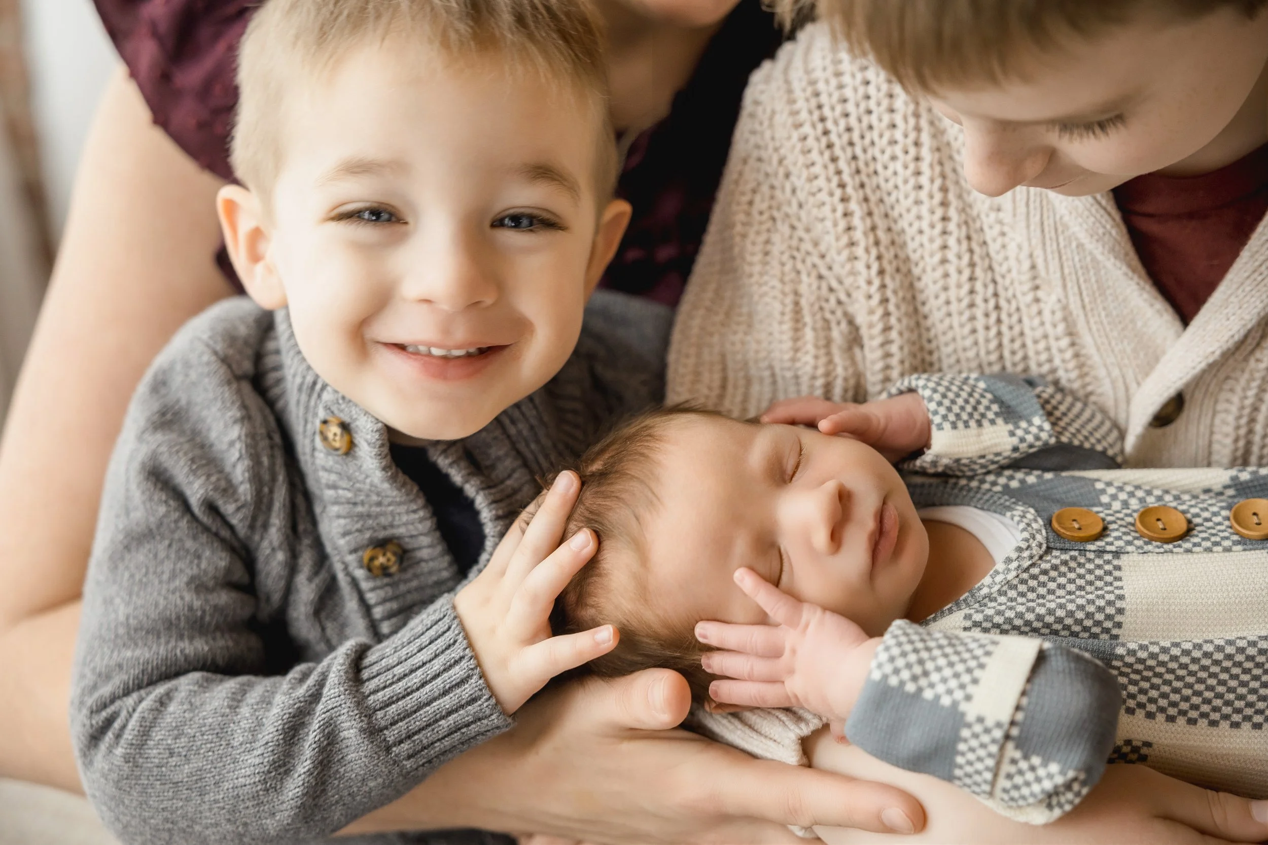 Kansas City newborn photography session in natural light studio featuring brothers holding their newborn sibling with parents standing behind in a neutral, timeless setup.