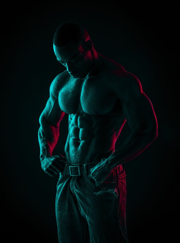 Low-key portrait of a bodybuilder's torso lit in red and teal