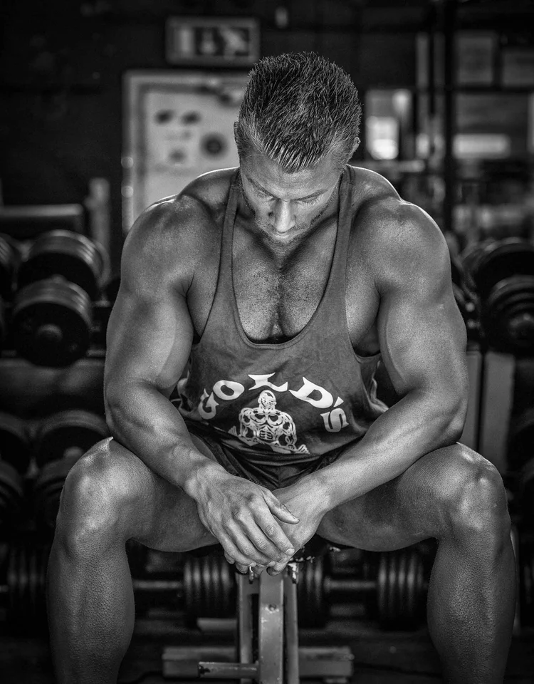 Black and white portrait of a muscular man sitting among dumbbells in a gym