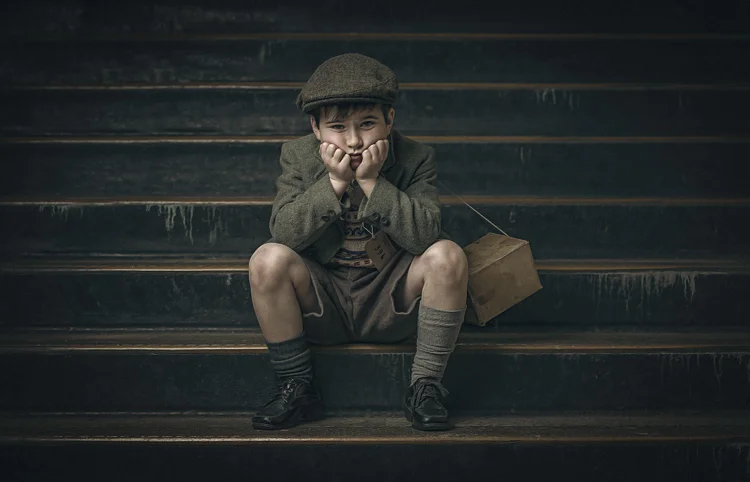 Boy in a flat cap sitting on wooden steps with his chin in his hands