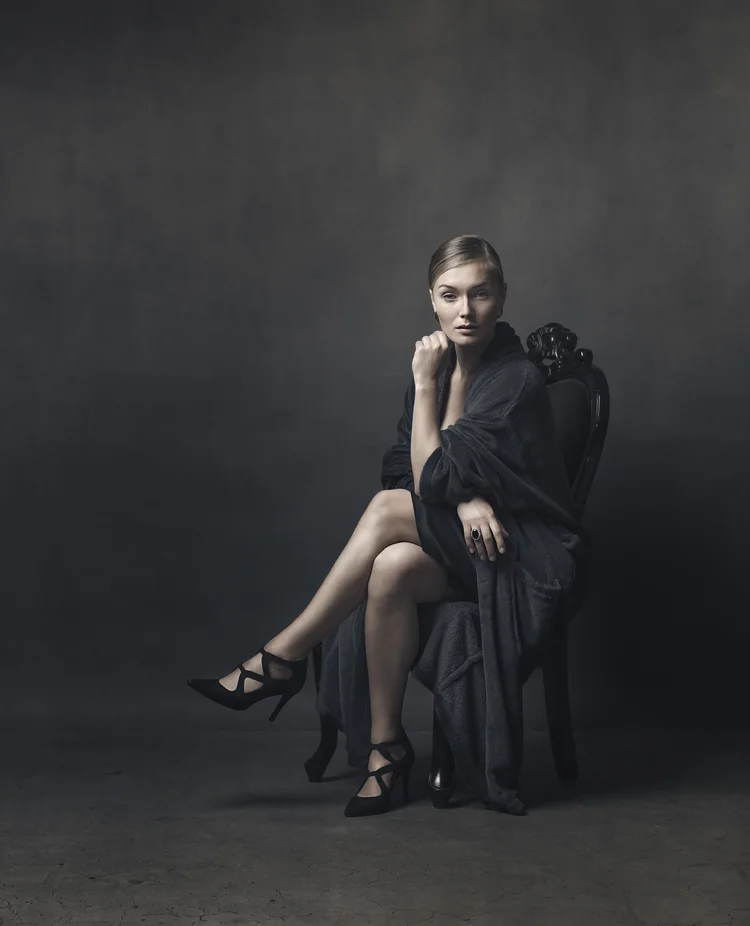 Woman in a black dress sitting on a stool, low-key studio portrait