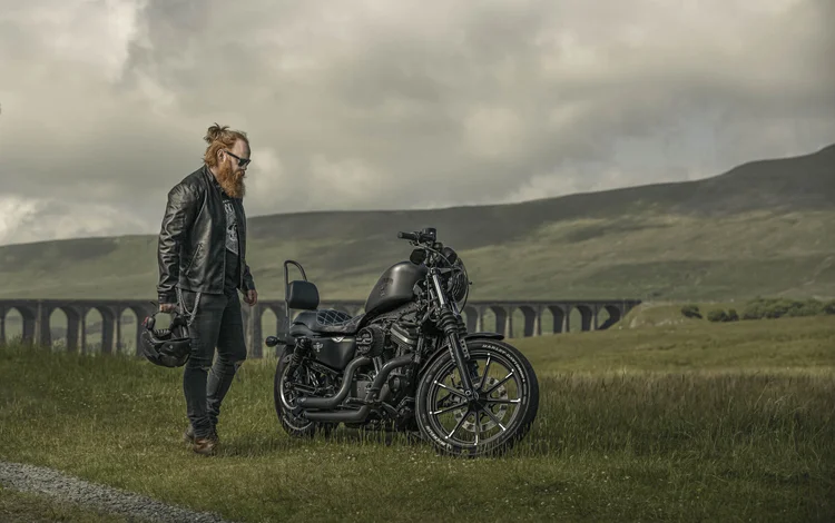 Woman standing beside her motorbike in front of a stone viaduct