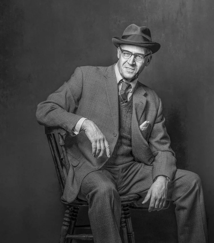 Black and white portrait of a man in a suit and trilby sitting on a chair