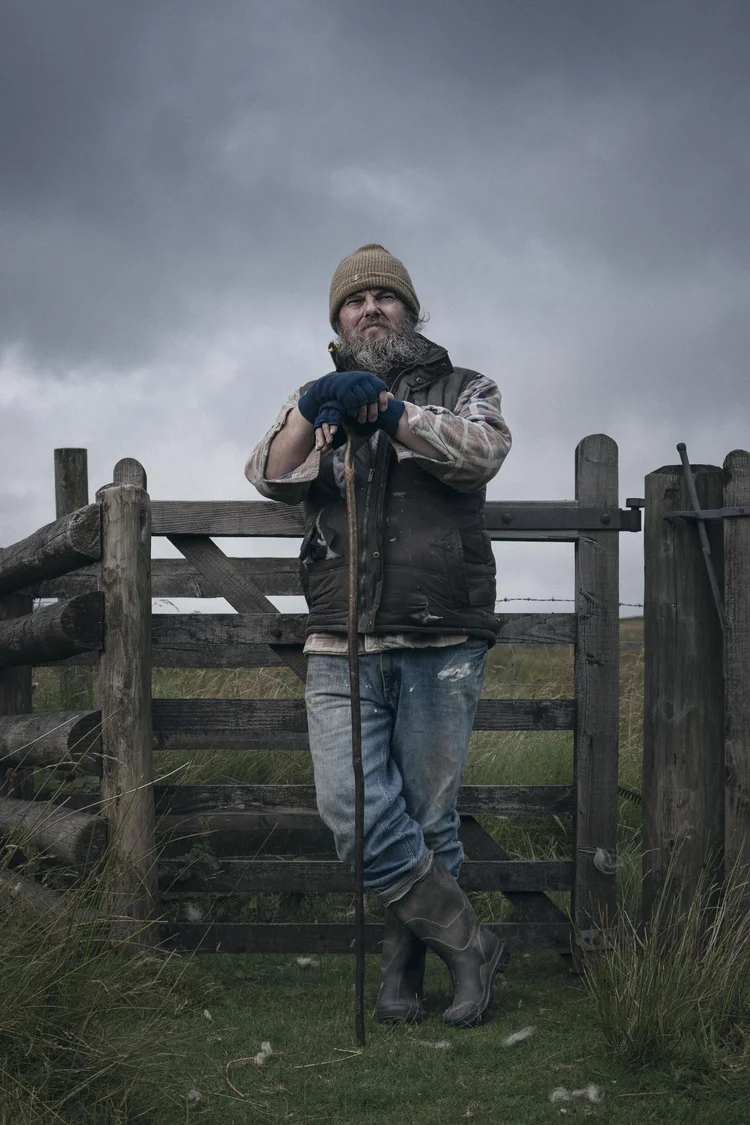 Man in a beanie leaning on a farm gate in the countryside