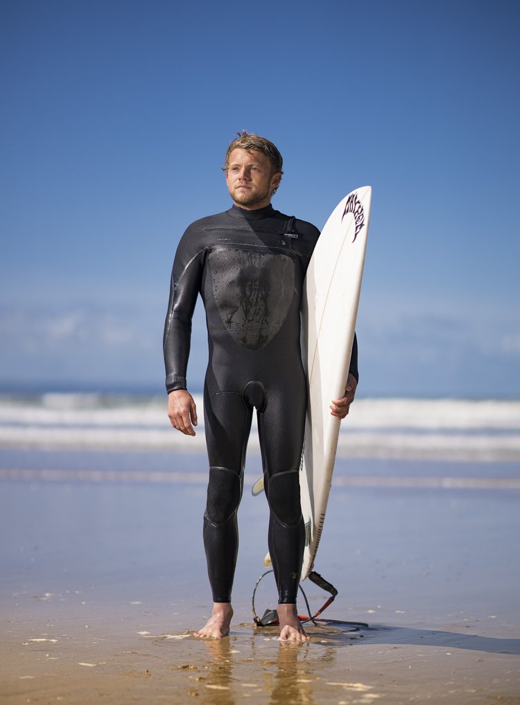 Surfer in a wetsuit holding a surfboard on the beach