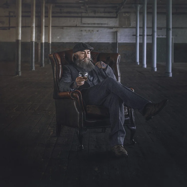 Bearded man in a tweed suit sitting in an armchair in an old industrial building