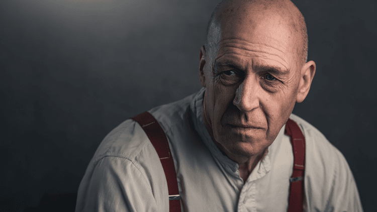 Bald man in a white collarless shirt and braces, cinematic portrait