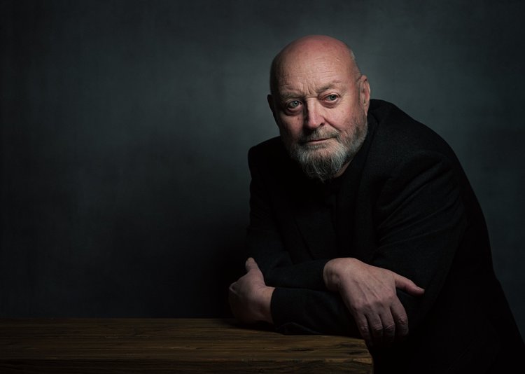 Bearded man in black leaning on a table, low-key studio portrait