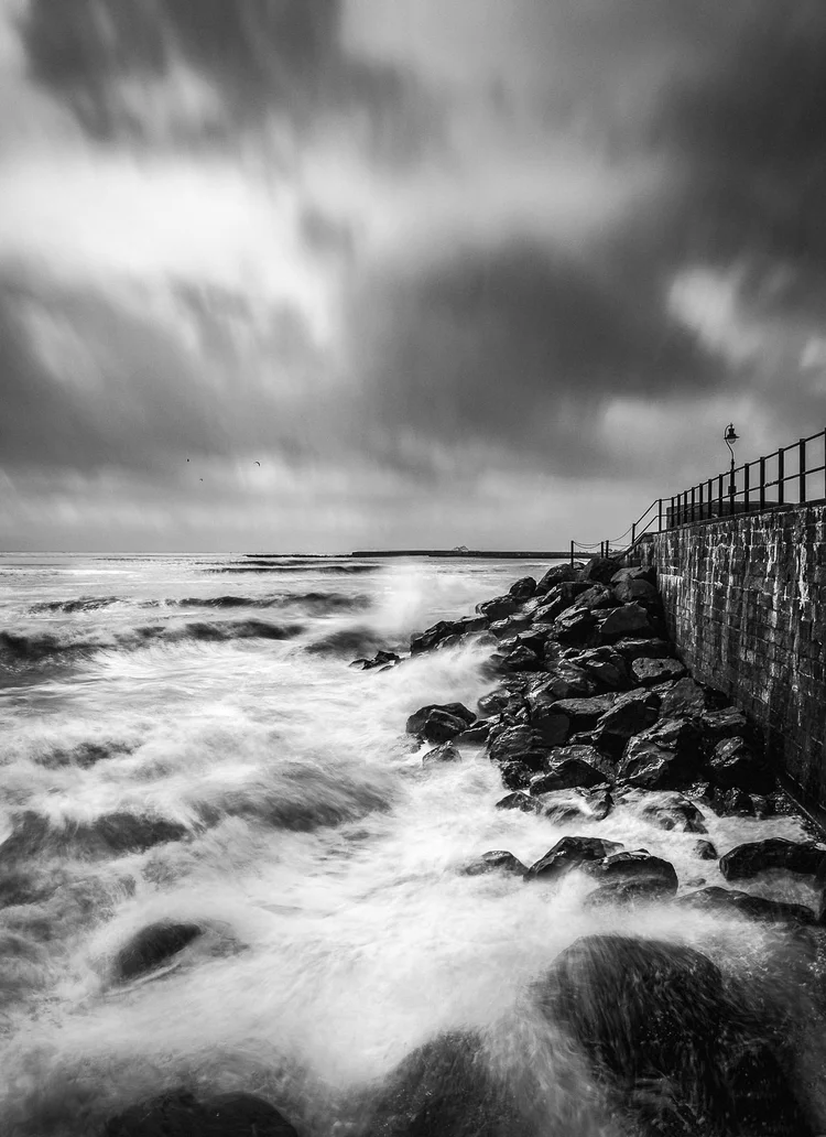 Black and white image of waves crashing on rocks beside a jetty at Lyme Regis