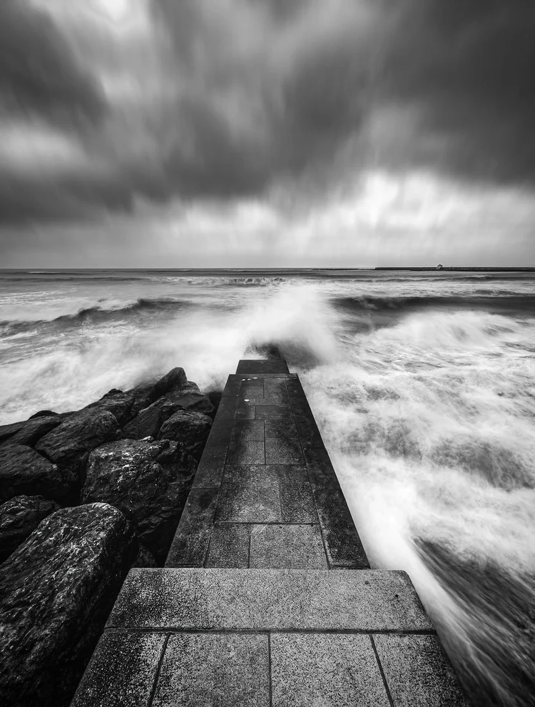 Black and white image of waves breaking over a breakwater at Lyme Regis
