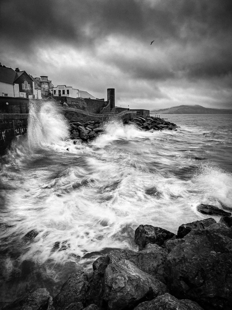 Black and white image of waves crashing over rocks at Lyme Regis