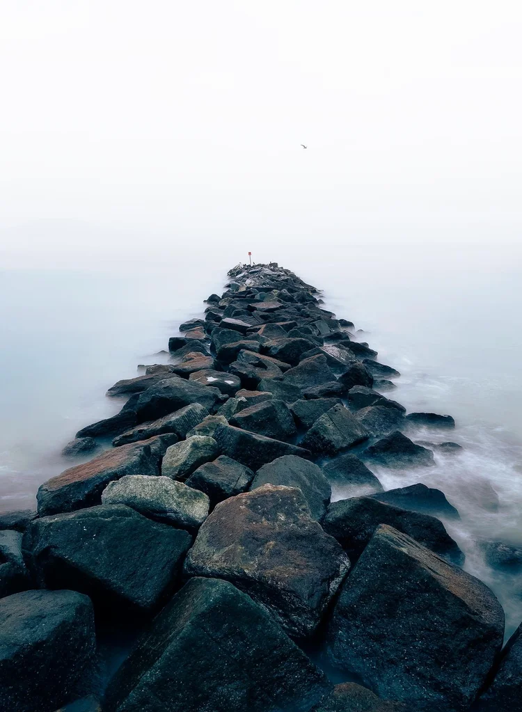 Long exposure of a rock groyne leading into a misty sea at Lyme Regis