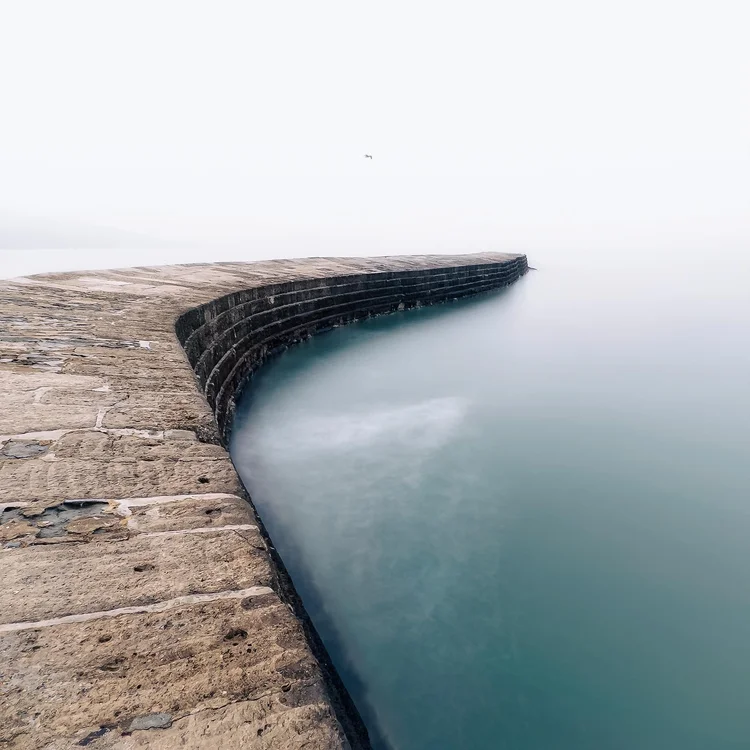 The Cobb at Lyme Regis curving into a calm, misty sea