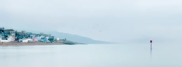 Lyme Regis seafront across a calm, misty sea