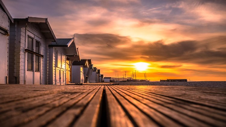Sunset along a row of beach huts and a wooden boardwalk at Lyme Regis