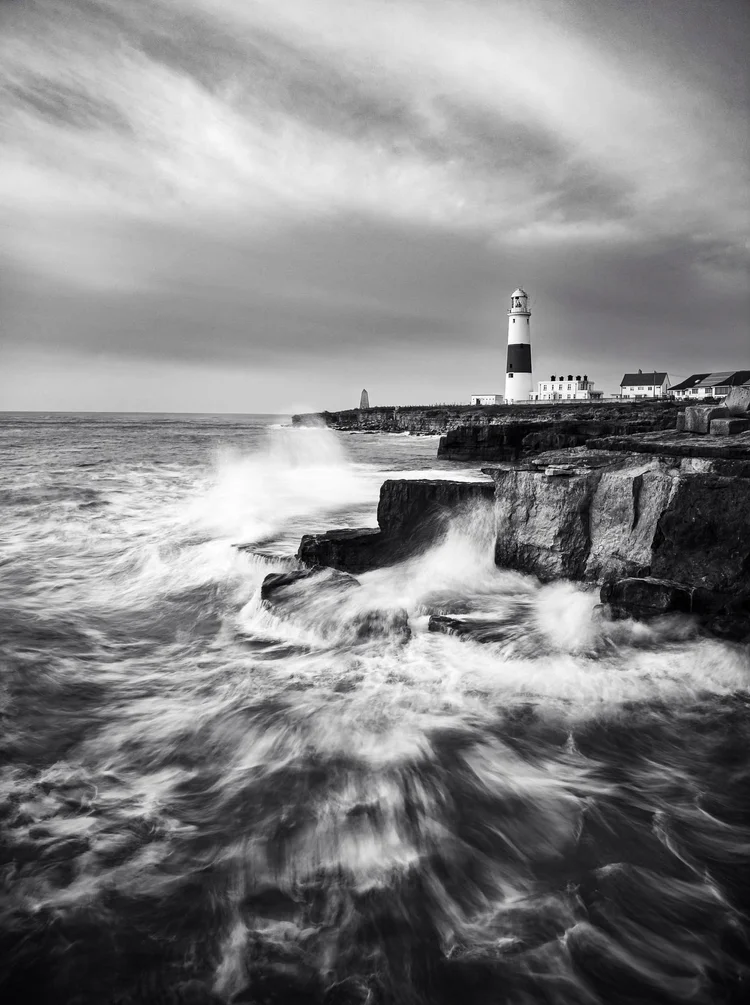 Black and white image of waves crashing below the lighthouse at Portland