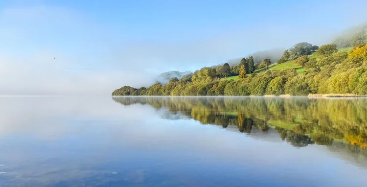 Misty lake reflecting a wooded hillside in Wales