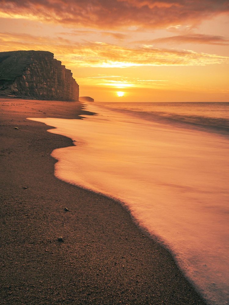 Sunset over the beach and golden cliffs at West Bay, Dorset