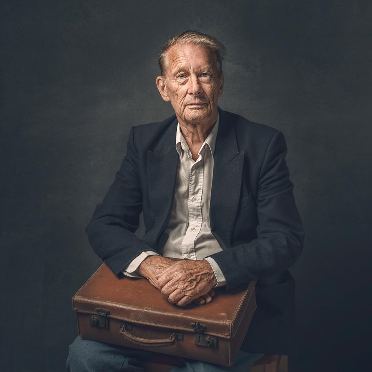 Elderly man in a blazer sitting with a leather briefcase on his lap