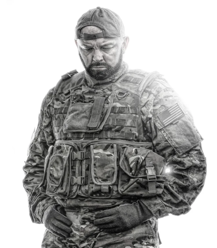High-key black and white portrait of a soldier in combat gear holding his helmet
