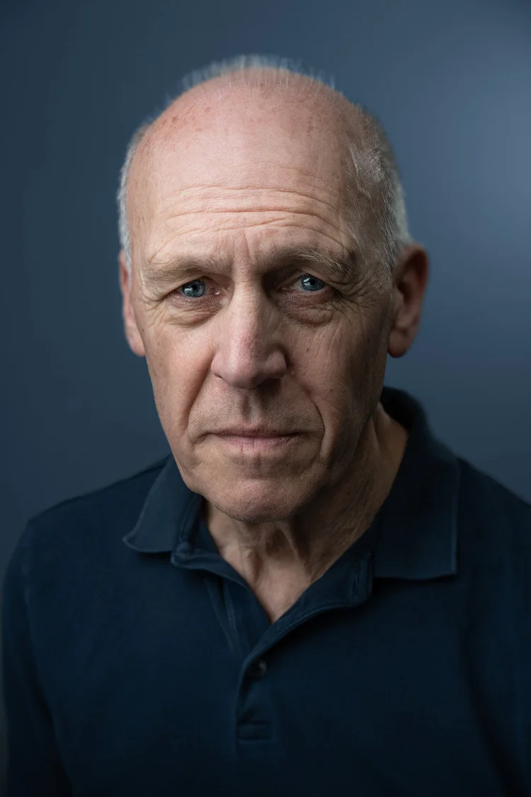 Older man in a navy polo shirt against a blue studio backdrop