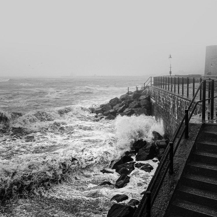 Black and white image of rough sea crashing against a sea wall