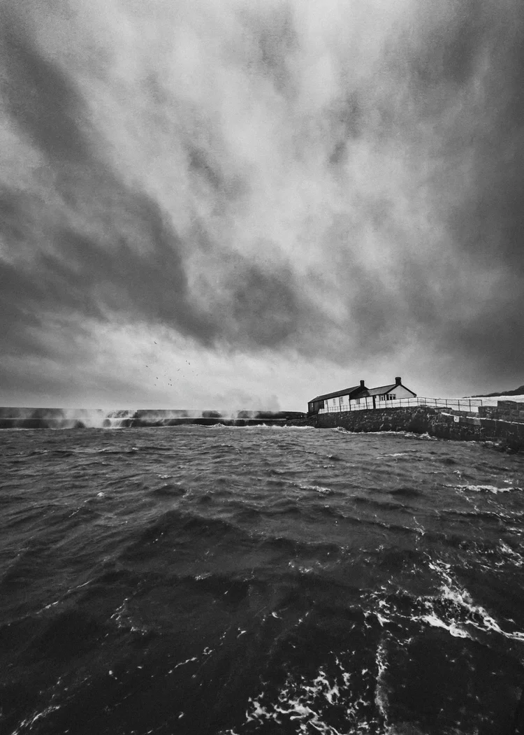 Black and white image of a stormy sea and headland under heavy cloud