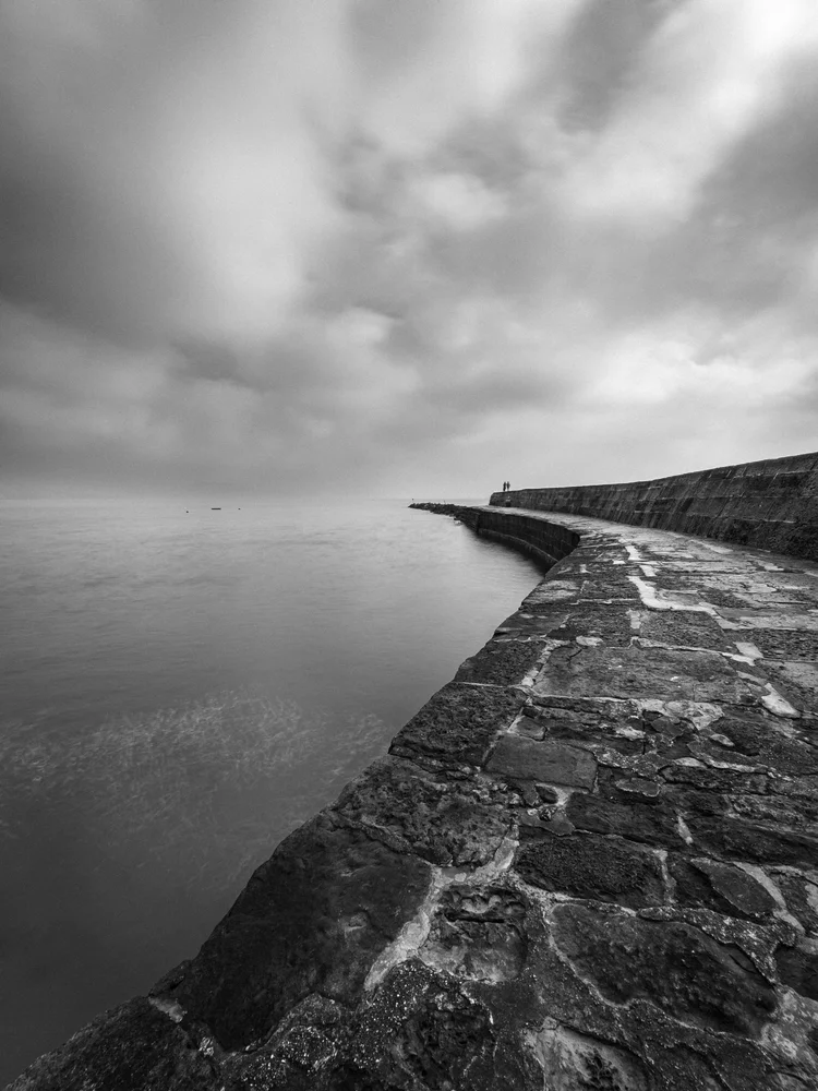 Black and white image of The Cobb harbour wall curving out to sea, Lyme Regis