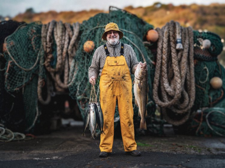 Fisherman in yellow oilskins holding fish in front of nets and ropes