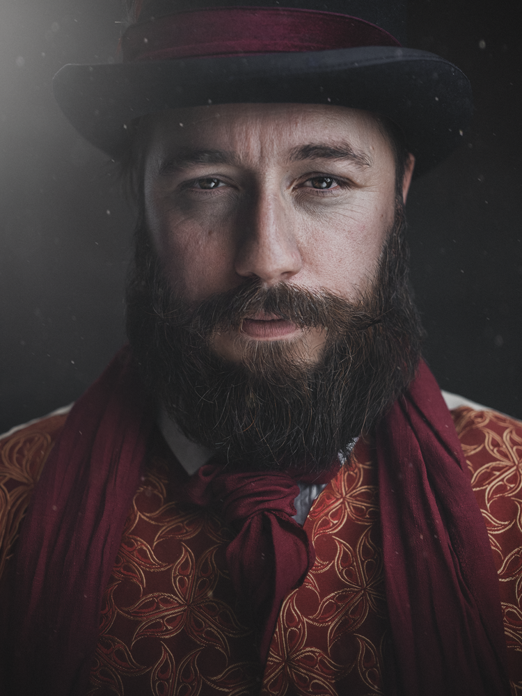 Bearded man in a top hat and red scarf, low-key studio portrait