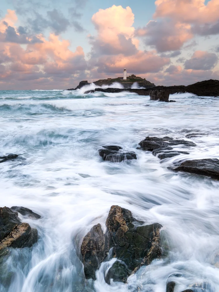 Long exposure of waves washing over rocks beneath pink clouds