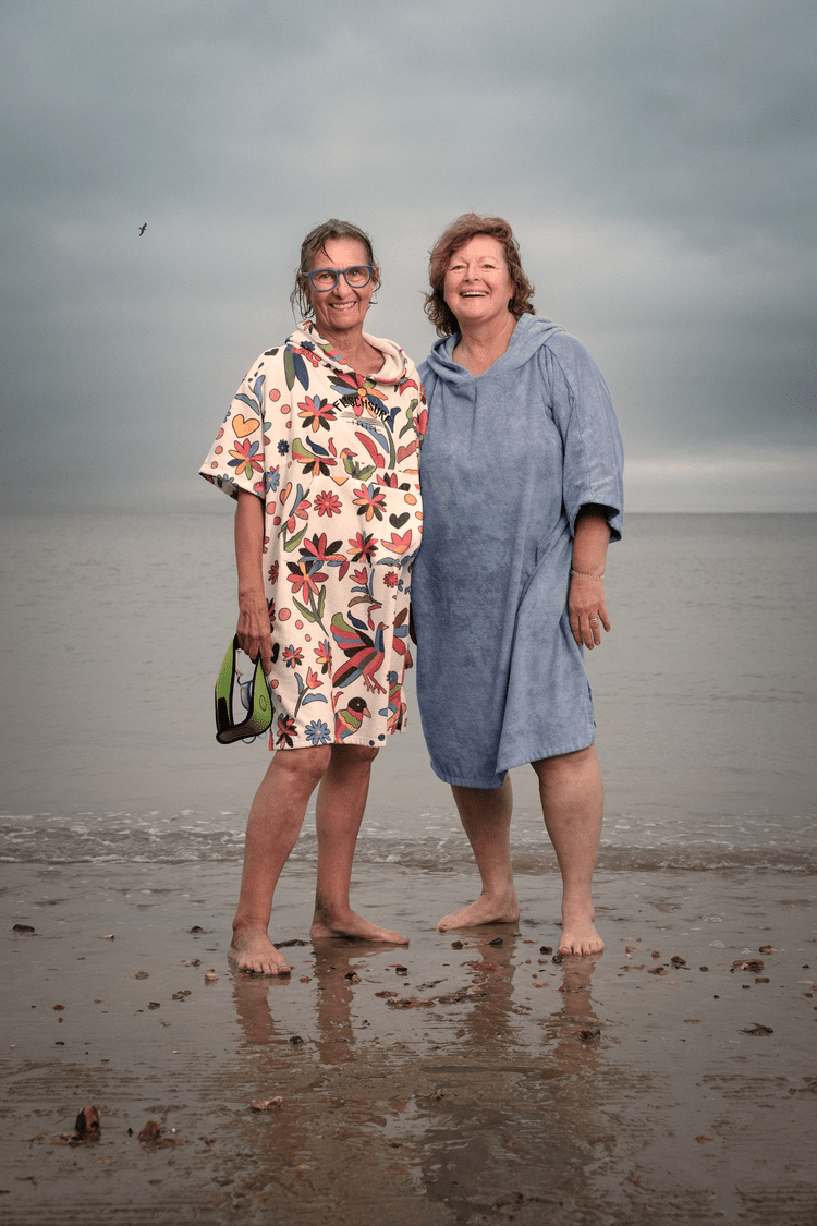 Two women standing barefoot together on wet sand at the water's edge