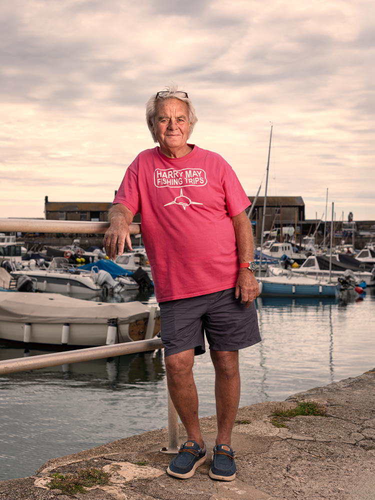 Man in a pink T-shirt standing on a harbour wall with moored boats behind him