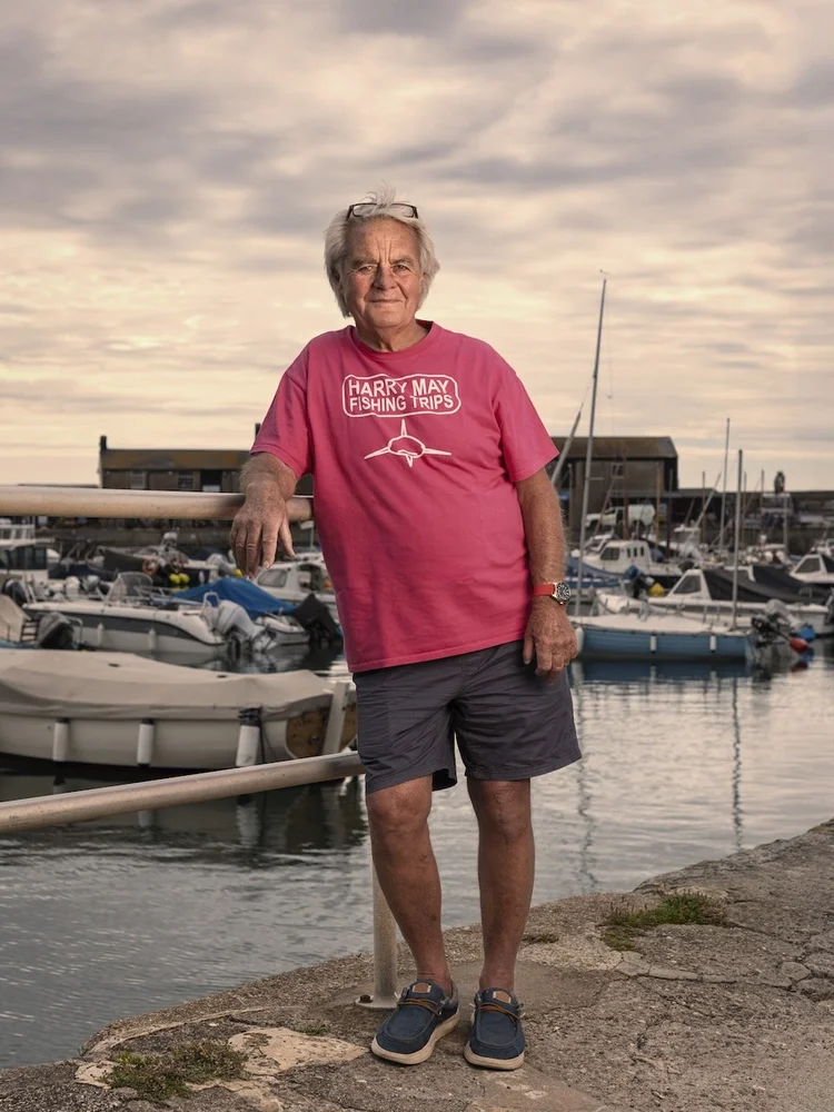Harry May in a pink T-shirt on the harbourside at Lyme Regis with boats behind