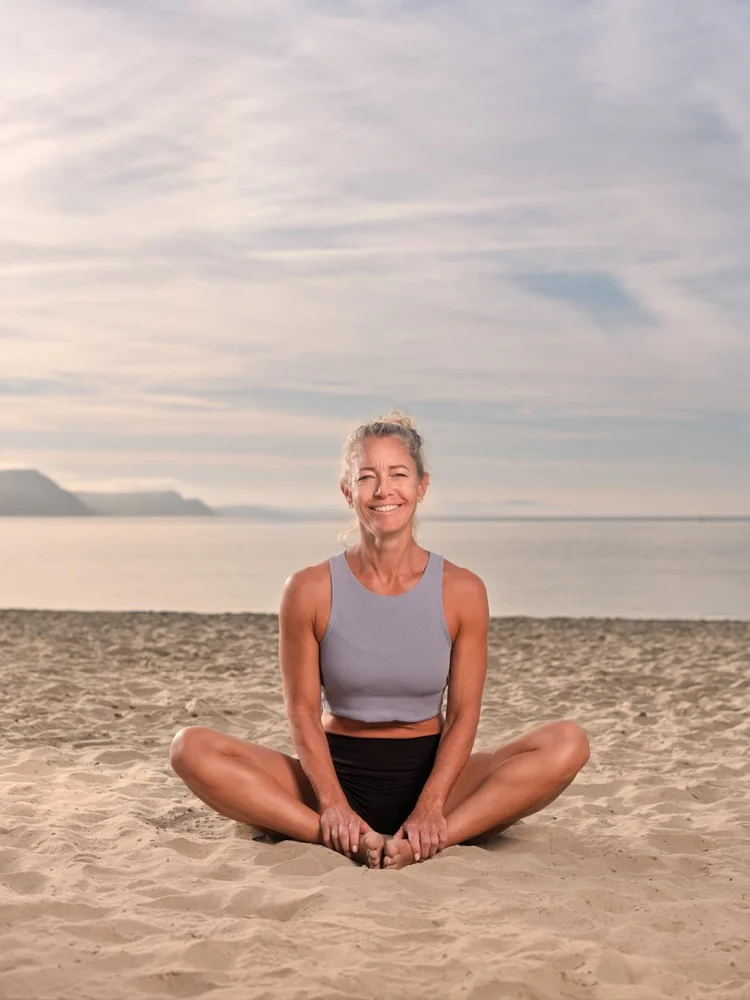 Yoga teacher Pip sitting cross-legged on the beach at Lyme Regis at sunrise
