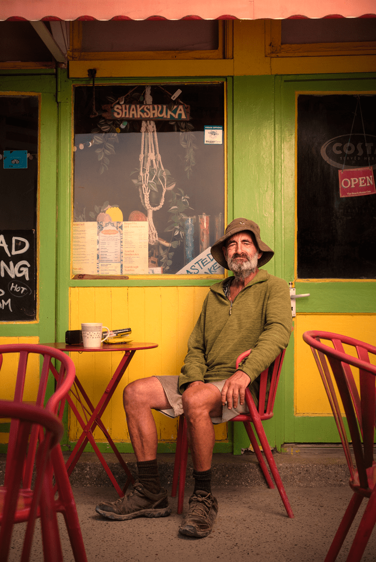 Jason in a bush hat sitting outside the brightly painted Beach House Cafe on the seafront