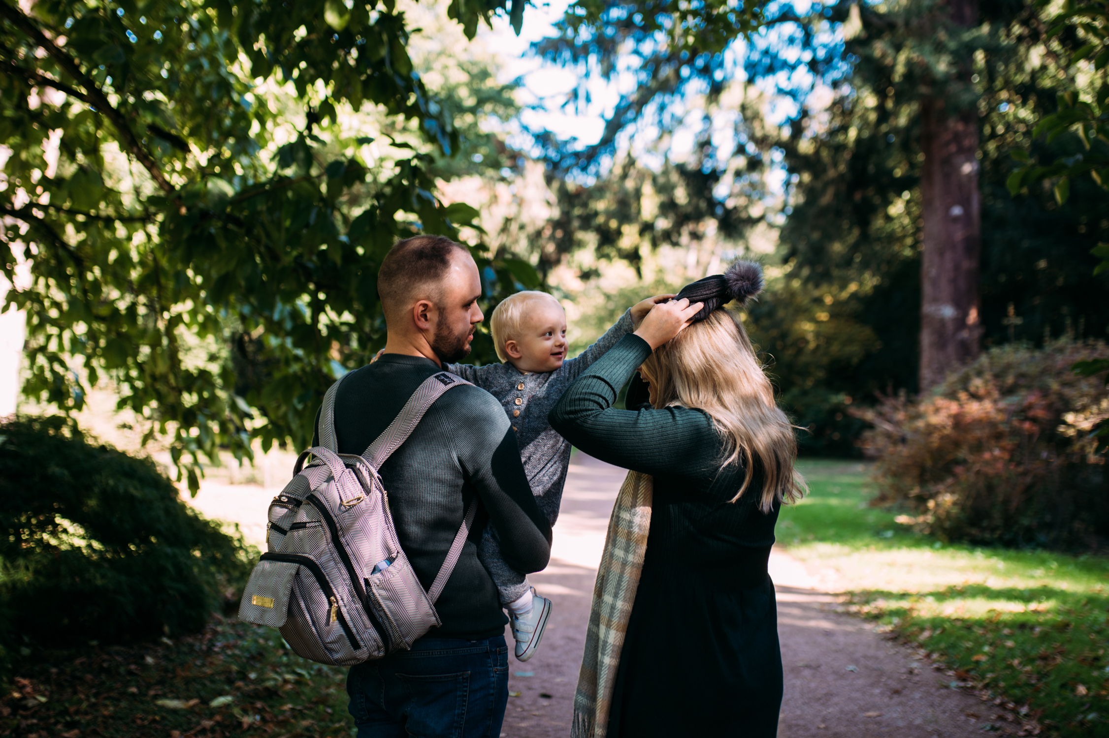 A toddler tires to put his hat on his mothers head as his father holds him during this autumnal family photo shoot at Westonbirt Arboretum.