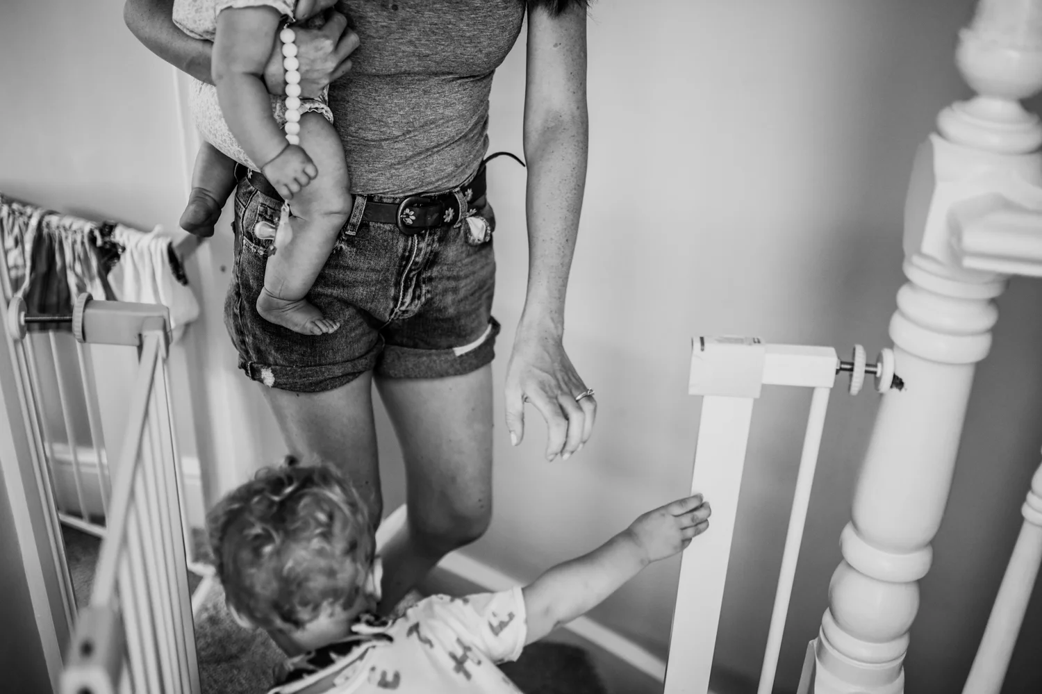 A mother walks down the stairs holding a baby in her arms and a toddler in front of her during this day in the life photo session in Yeovil, Somerset.