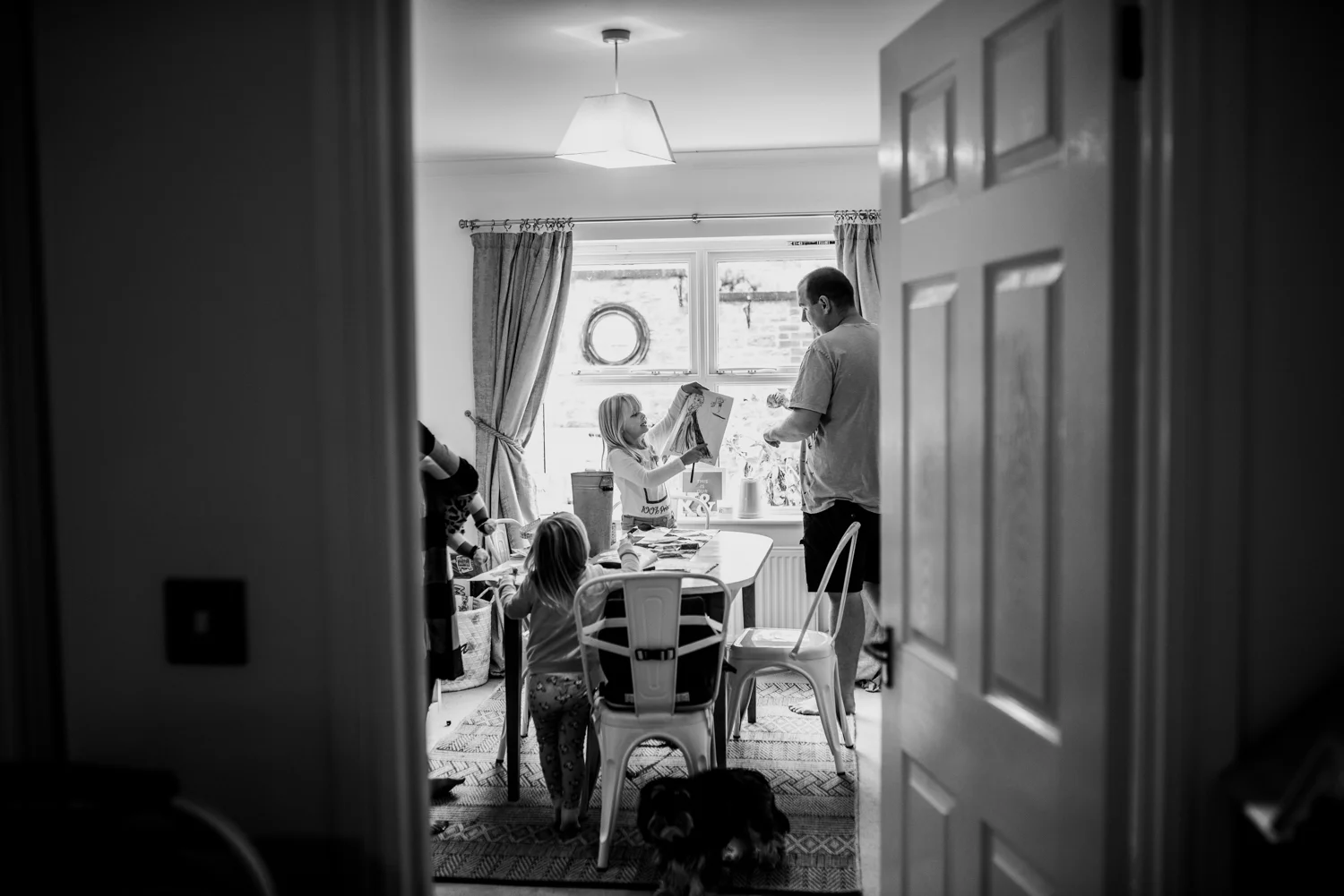 A shot through a door frame of daughter showing her father a picture she has drawn during this relaxed at-home photo session in Somerset.