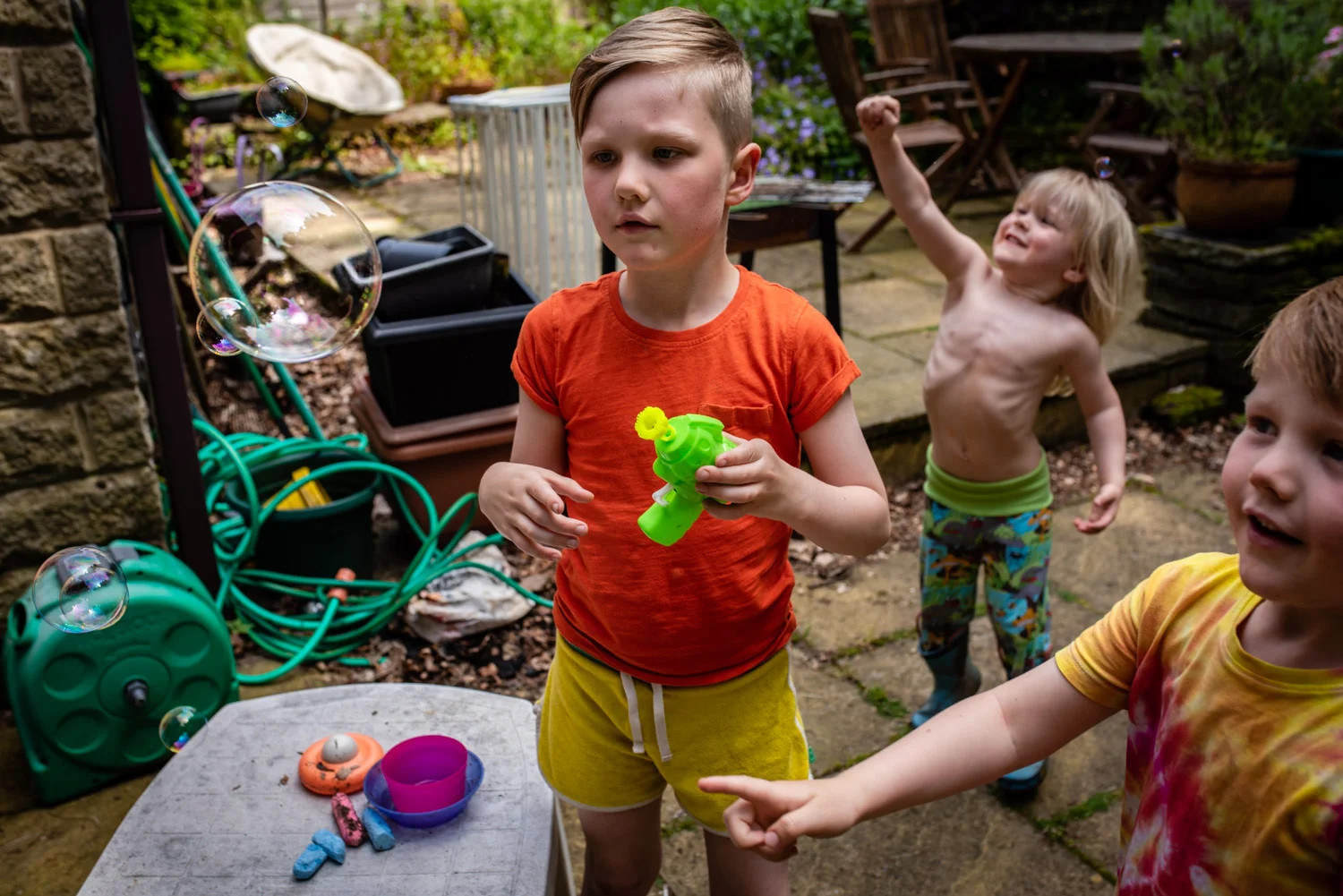 Three young brothers stand in their garden blowing and catching bubbles during this unposed family photo shoot in Manchester, UK.