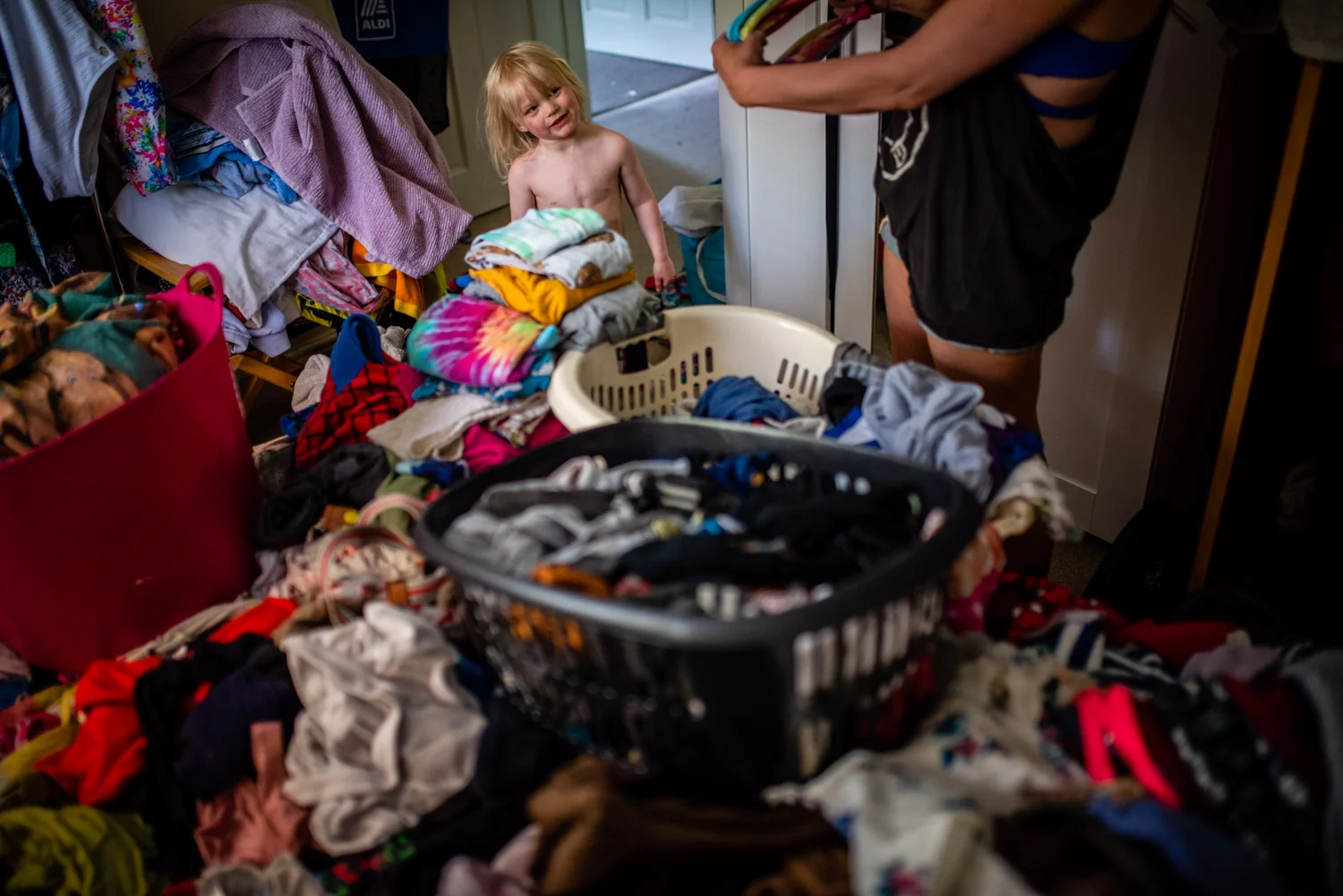 A mother sorts through the laundry whilst her little toddler boy looks on curiously, during this unposed family photo shoot in Manchester, UK.