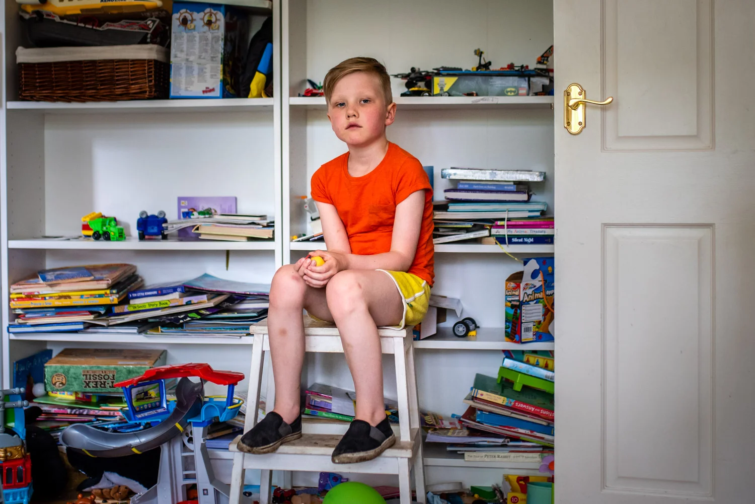A portrait of a young boy sat on a stool in his play room surrounded by toys during this relaxed family photo shoot in Manchester, UK.